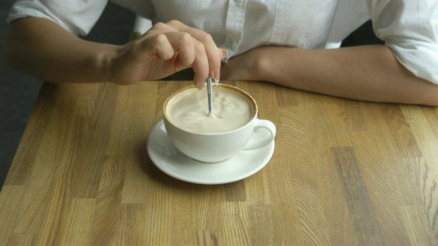 一个年轻漂亮的女人在咖啡馆喝咖啡。女孩的手在咖啡里搅拌糖视频素材
