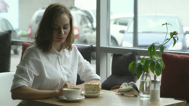 那个女孩坐在咖啡馆里享受着香浓的咖啡和香甜的蛋糕。在休息期间休息的女商人视频素材