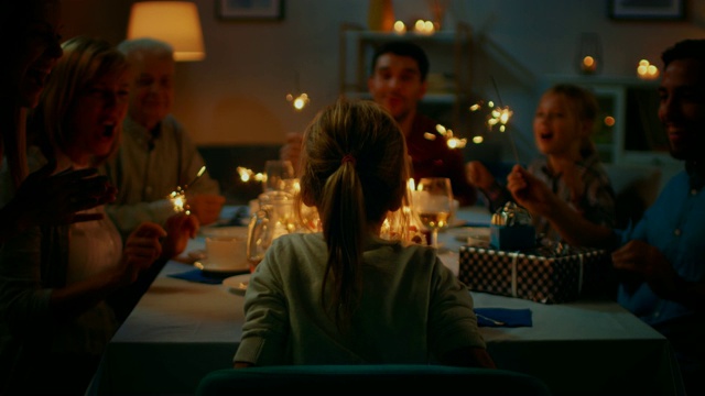 后景拍摄:可爱的小女孩在餐桌上吹灭蛋糕上的蜡烛庆祝生日。在餐桌上，亲朋好友欢聚一堂。视频素材