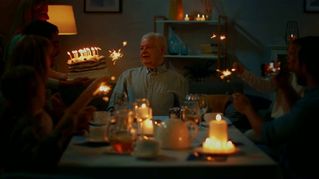 这是一个女儿给她的父亲带来生日蛋糕和蜡烛的照片。家庭聚餐和庆祝，人们聚在晚餐桌上。视频素材