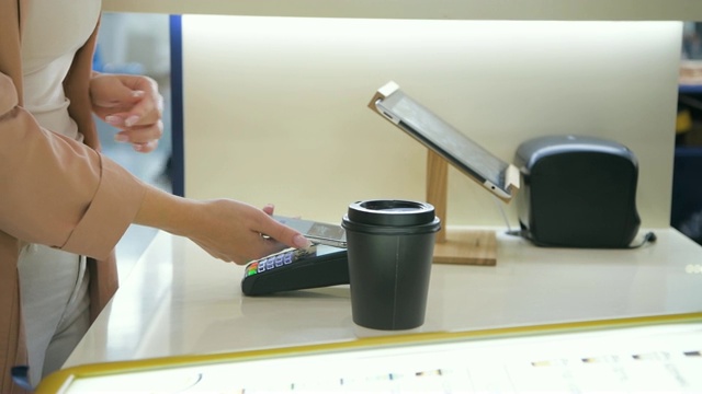 男人的手的特写，正在为顾客做外卖咖啡，顾客通过带有人脸识别功能的现代非接触式手机向信用卡系统终端付款视频素材