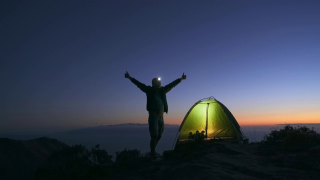 黄昏时分，快乐的游客在山顶搭起帐篷，准备在户外过夜视频下载