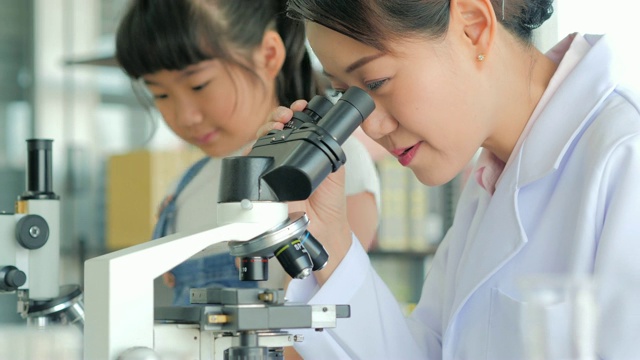 亚洲小孩和老师在学校实验室用显微镜观察。小女孩用显微镜学习科学课。教育的主题视频素材