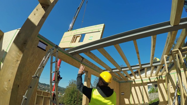 工头向操作吊车的工人发出信号，让他们为预制房屋移动一堵木墙视频素材