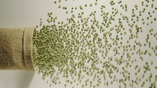 慢动作:绿色的豌豆从掉落的袋子里倒出来-俯视图视频素材