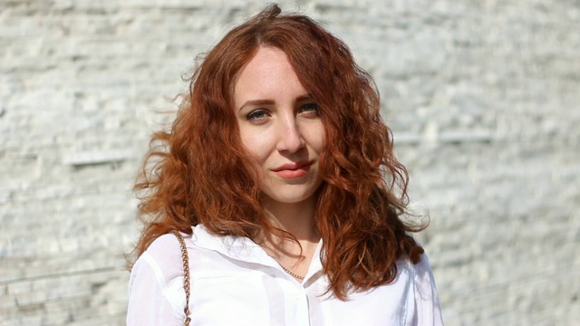 一个快乐的长头发红发女孩的肖像站在户外看着相机。视频素材