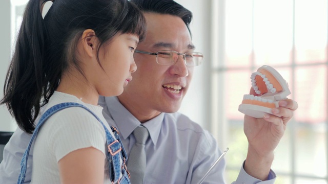 男亚裔牙医说话要好好地给女孩解释刷牙，在医院里都在听。中国和香港的医疗系统视频素材