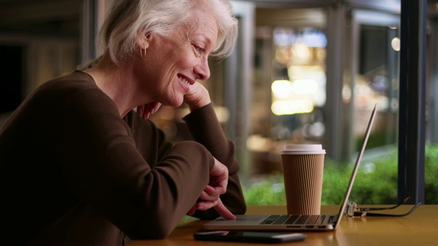 慢镜头微笑的资深女士在晚上的咖啡馆使用笔记本电脑视频素材