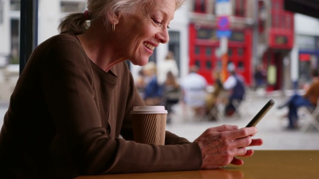 快乐的高级妇女收到好消息通过短信，而等待在咖啡店视频素材