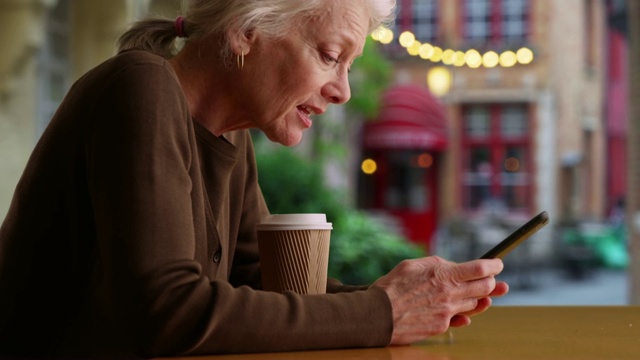 微笑的年长白人妇女在咖啡厅露台上与朋友发手机短信。视频素材