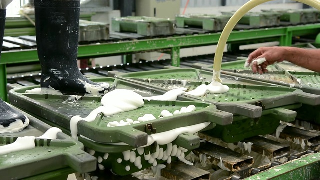 在橡胶枕厂的生产线上，工人将乳胶泡沫放入金属枕模的传送带上视频下载