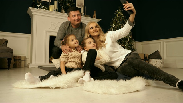 家庭、假期、科技和人——微笑的妈妈、爸爸和小女孩在圣诞树灯光背景下用相机自拍视频下载