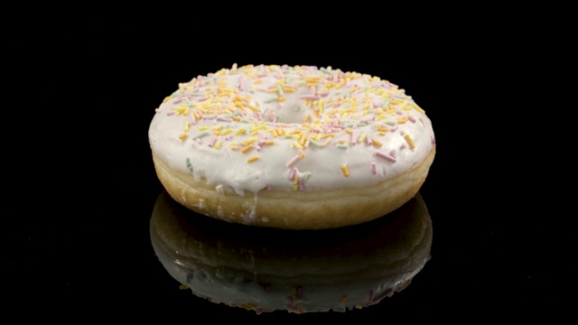 旋转的甜甜圈与白色糖衣在黑色的背景视频素材