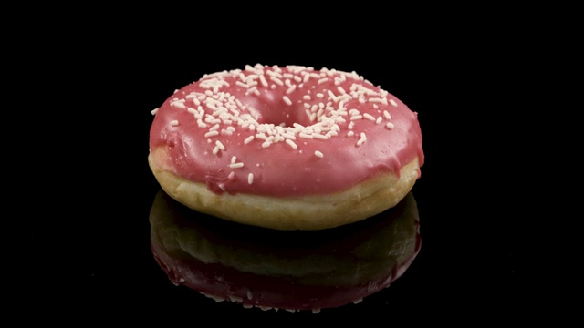 在黑色背景上旋转粉色糖衣的甜甜圈视频素材
