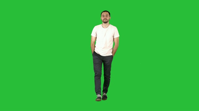 一个自信的年轻人向前走着，在绿色屏幕上穿着白色衬衫看着摄像头视频素材