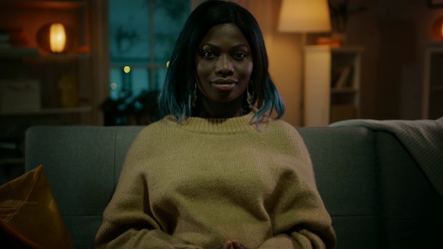 一个漂亮的黑人女孩晚上坐在家里的沙发上，看电视上的恐怖电影。她变得非常害怕和情绪化。视频下载
