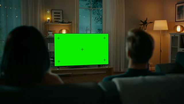 一对夫妇坐在客厅的沙发上看绿色模拟屏幕电视。男女朋友的浪漫之夜。视频素材