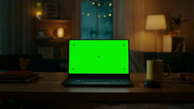 在客厅的桌子上有一台绿色键盘的笔记本电脑。在背景舒适的客厅在晚上与温暖的灯。放大照片。视频素材