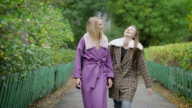 秋日里，两个快乐的女性朋友穿着暖和的外套在公园的巷子里散步聊天视频下载