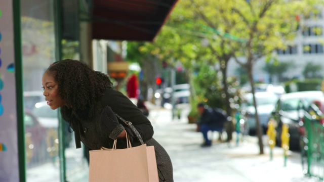 漂亮，时尚的黑色女性携带购物袋看着橱窗展示视频素材