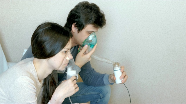 使用喷雾器和吸入器进行治疗。男人和女人通过吸入器口罩吸入。侧视图。视频下载
