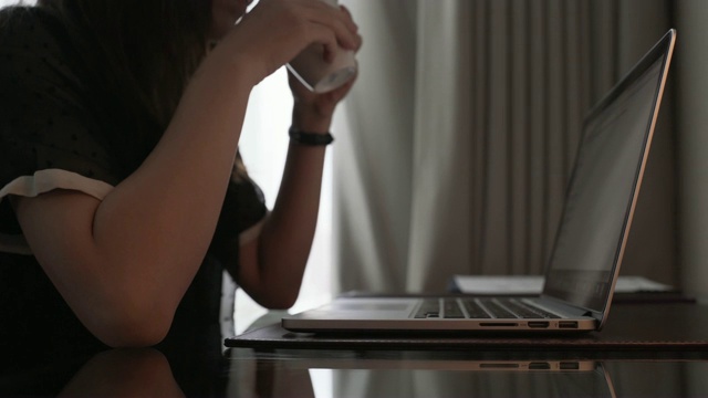 年轻女子在笔记本电脑上打字，然后拿起一杯咖啡视频素材