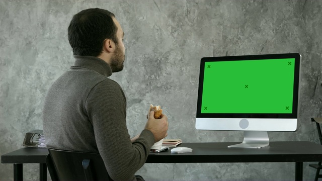生意人在办公室里吃着早餐，午餐，看着电脑上的东西。绿屏模拟显示视频素材