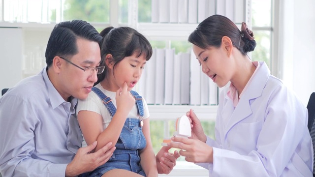 医学、牙科和保健概念-牙医在牙科诊所向儿童病人和她的父亲展示牙齿模型。中国和香港的医疗系统视频素材