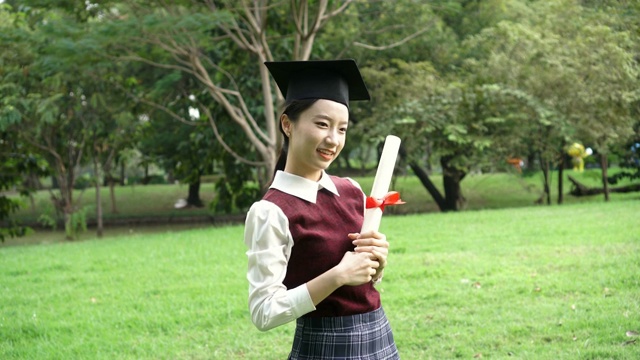 年轻迷人的亚洲女性新毕业生在学校制服摆姿势的照片在公园户外-成功和毕业的概念视频素材
