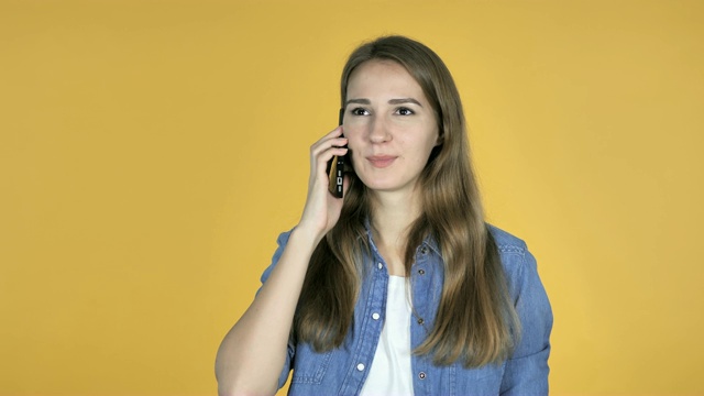 在黄色背景下用智能手机聊天的漂亮女人视频素材