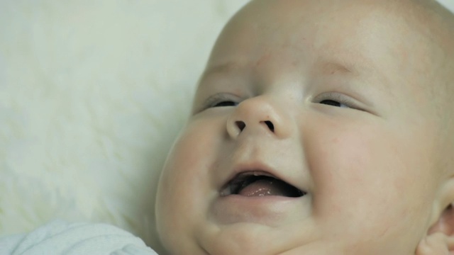 一个快乐的5个月的婴儿平静地躺在白色的毯子上，微笑着视频素材
