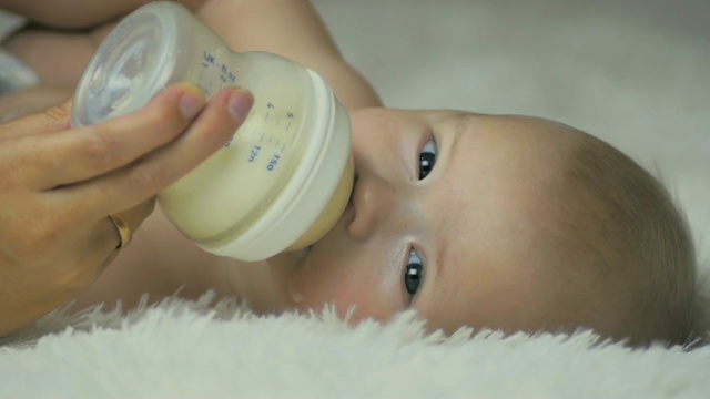 妈妈躺在白色的毯子上给她的新生儿喂奶。视频下载