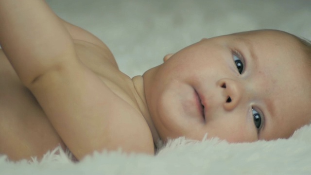 一个5个月大的婴儿躺在白色的毯子上，看着慢镜头。视频素材