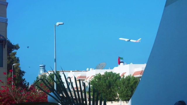 在一个晴朗的清晨，一架飞机飞过，阿拉伯联合酋长国的国旗在一所房子上方飘扬视频素材