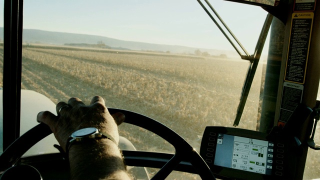 一个戴着手表的农民的手从拖拉机驾驶室里驾驶着拖拉机方向盘，用GPS在玉米地里导航视频素材