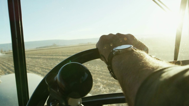 一个戴着手表的农民的手从拖拉机驾驶室里驾驶着拖拉机方向盘，在玉米地里导航视频下载