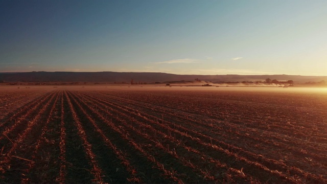 在科罗拉多西部晴朗的蓝天下，一架卡车返回的无人机拍摄了日落时分尘土飞扬的玉米田，背景是拖拉机和群山视频购买
