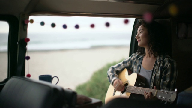 一个年轻女子在海滩边的露营车里弹吉他视频下载
