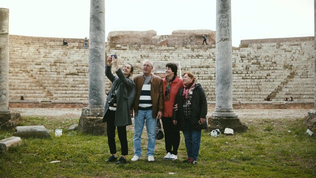 微笑的年轻欧洲女孩和快乐的高级旅游团在奥斯蒂亚，意大利古老的圆形剧场遗址附近自拍。视频下载
