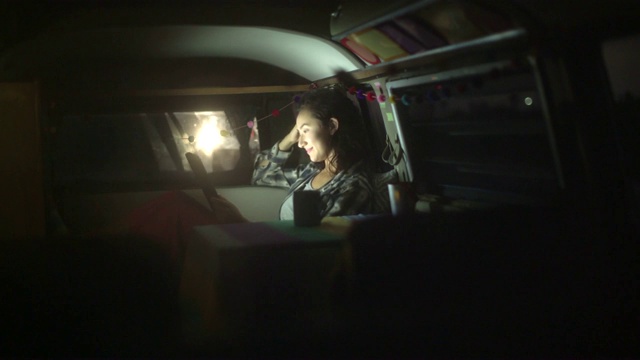 一个年轻女子坐在她的露营车里用笔记本电脑看电影视频下载