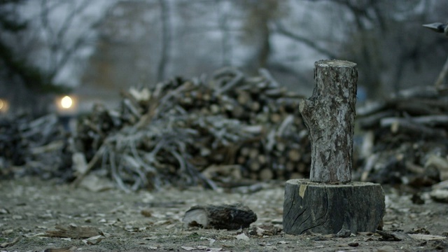 一个戴着防护手套的人在一个阴天的黄昏时分，用斧头把一根木头劈成两半做柴火视频素材