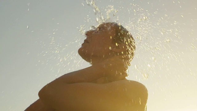 近距离拍摄的一个年轻的金发女人在一个热带户外淋浴在日落。视频下载