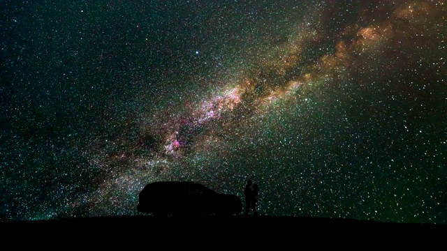 一个男人和一个女人站在一辆汽车旁，映衬着星空。时间流逝视频素材