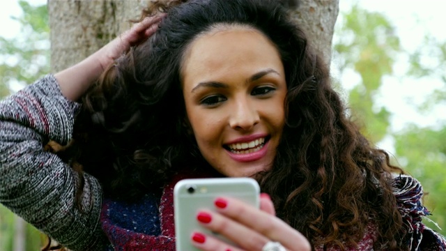 一名年轻漂亮的女子在公园里用智能手机自拍视频素材