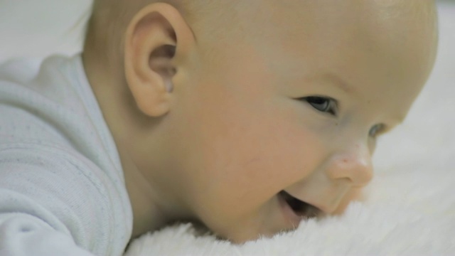 一个新生儿的特写镜头，躺在他的腹部在一个白色的毯子和微笑的慢动作。视频素材