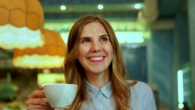 美丽的女人用杯子喝着卡布奇诺咖啡，对着镜头微笑视频素材