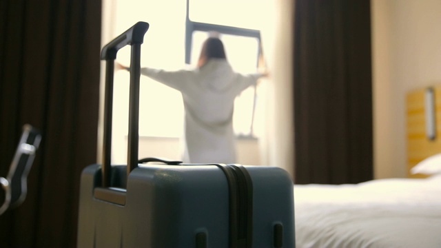 一个女人拿着行李在酒店房间里拉开窗帘视频素材