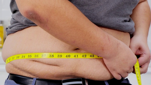 超重男子用卷尺检查自己超重。健康的概念。真实的身体视频素材