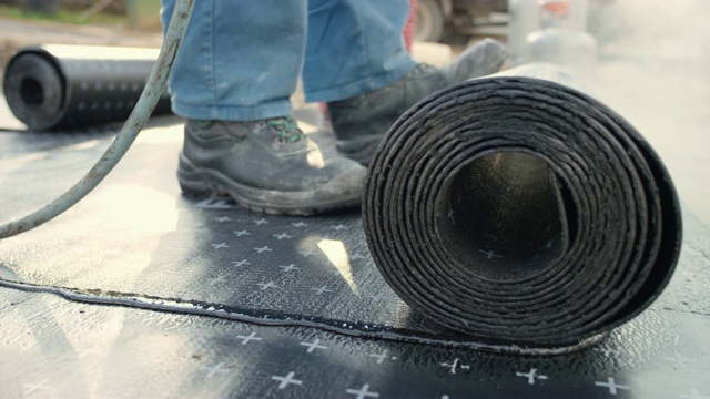 建筑工人在混凝土表面上滚动加热的沥青卷视频素材