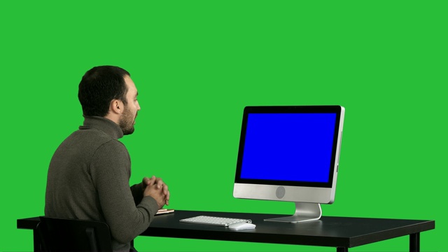 年轻的商人在他的电脑上进行视频通话在绿色屏幕上，色度键。蓝屏模拟显示视频素材